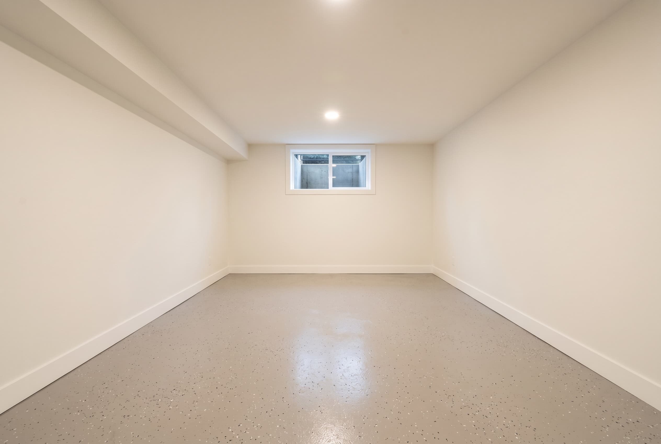 Wide finished empty Troy basement with warm grey epoxy floor.